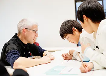 机を挟んで、外国人講師と子どもたちがコミュニケーションをとっている様子。